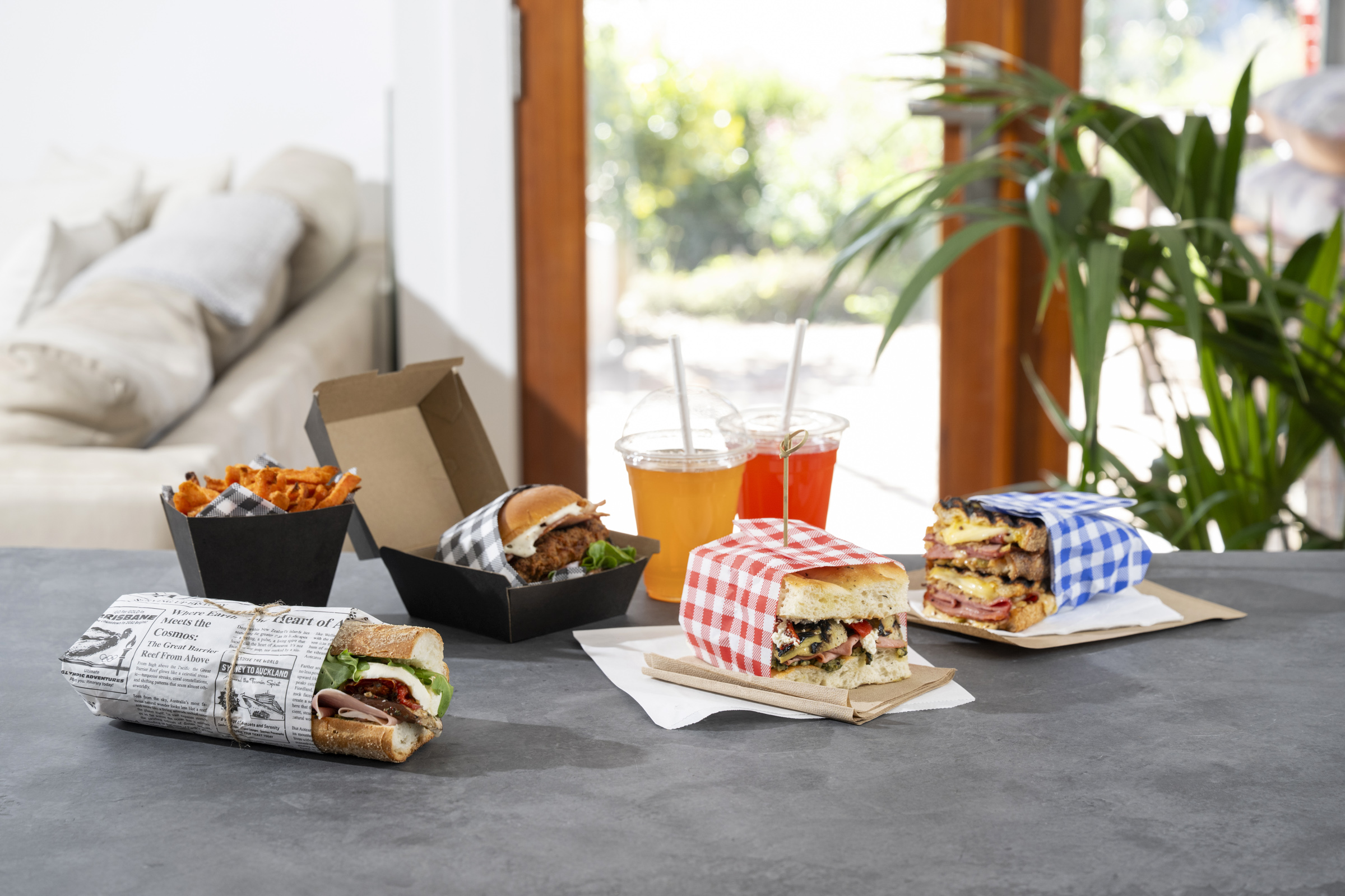 Detpak Greaseproof Wrap dispenser with black gingham paper, next to sandwiches and fries in colored gingham wraps.